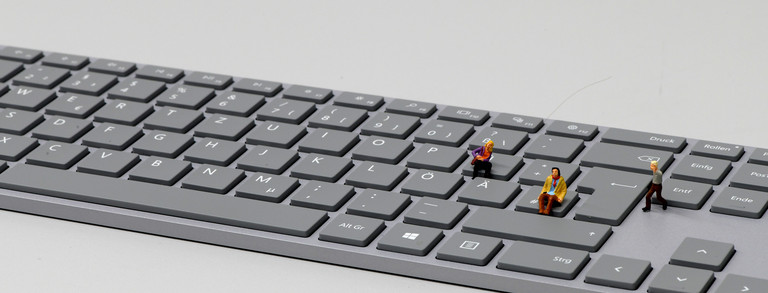 Zwei sitzende und ein laufender Miniaturmensch auf einer Tastatur