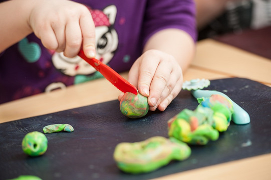 close-up of a child cutting green modeling clay with a red plastic knife