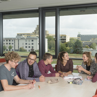 Studierende sitzen mit Lernunterlagen am Tisch.