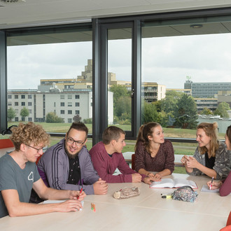 Studierende sitzen mit Lernunterlagen am Tisch.