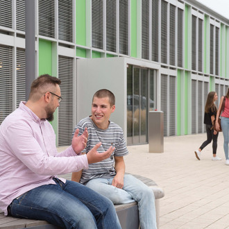 Studierende sitzen vor einem Gebäude.