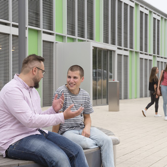 Studierende sitzen vor einem Gebäude.