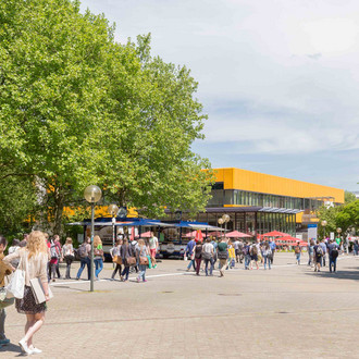 Studierende auf dem Campus Nord mit der Hauptmensa im Hintergrund im Sommer