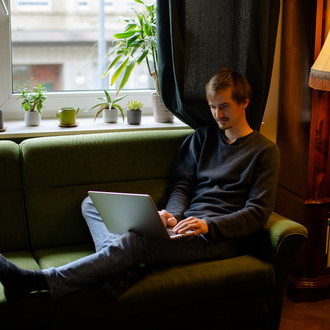 Ein Student, auf dem Sofa sitzend, arbeitet am Laptop.