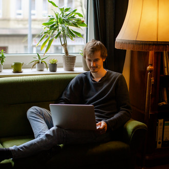 Ein Student, auf dem Sofa sitzend, arbeitet am Laptop.