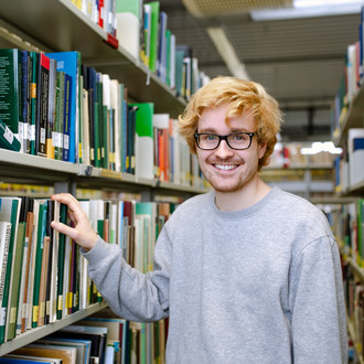 Studierender steht an einem Bücherregal in der Bibliothek.