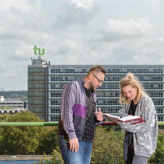 Ein Student und eine Studentin sehen in ein Buch, im Hintergrund ist der Mathetower zu sehen.