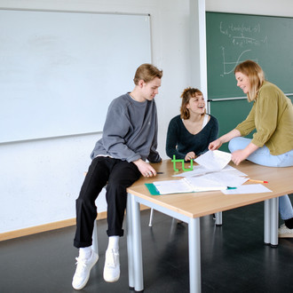 Drei Studierende im Seminarraum sitzen um einen Tisch herum und arbeiten gemeinsam.