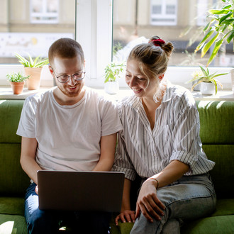 Zwei Studierende arbeiten am Laptop, auf einem Sofa sitzend.