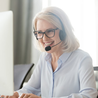 Eine Frau sitzt vor ihrem Laptop und trägt ein Headset. 