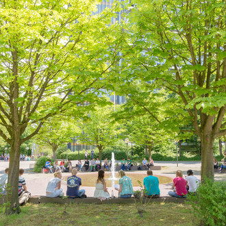 Studierende sitzend am Springbrunnen auf dem Campus Nord im Sommer