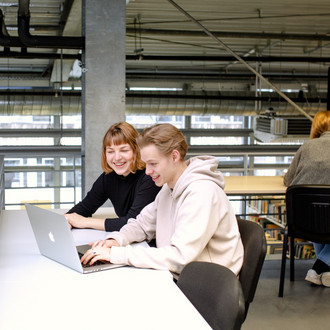 Zwei Studierende sitzen in der Bibliothek am Tisch und arbeiten an einem Laptop