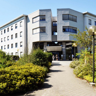 Maschinenbau-Gebäude I: Ein großes weißes Gebäude mit zwei Flügeln. Davor ein Weg, der von Büschen gesäumt ist. Links im Bild ein Schild mit der Aufschrift "Maschinenbau, Leonhard-Euler-Straße 5".