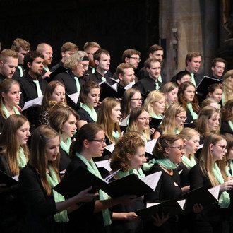 Ein Chor steht in einer Kirche, hält Gesangsbücher in der Hand und singt.