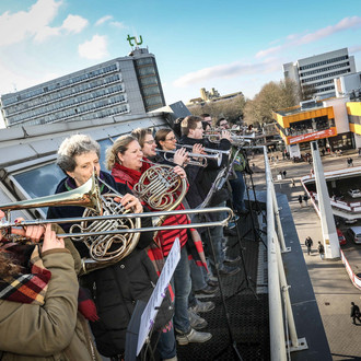 Eine Gruppe Blasmusikerinnen und -musiker steht auf dem Dach der Bibliothek und gibt ein Konzert.