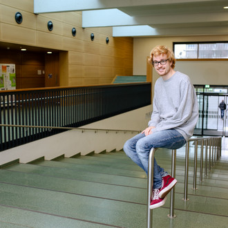 Student sitzt auf einem Geländer an der Treppe und schaut gerade aus.