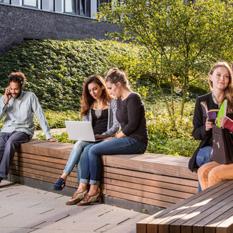Studierende sitzen auf einer Sitzgruppe hinter dem neuen Physikgebäude