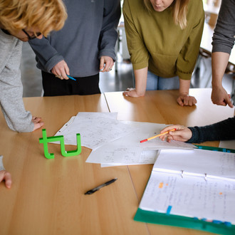 fünf Studierende stehen um einen Tisch und lesen ein Dokument.