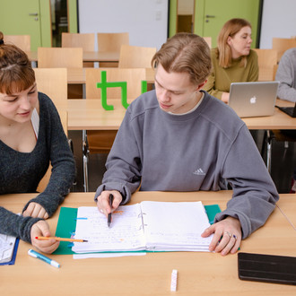 Zwei Studierende im Seminarraum arbeiten zusammen an Unterlagen.