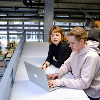  Zwei Studierende sitzen an einem Tisch in der Bibliothek und arbeiten.