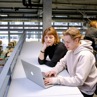Zwei Studierende sitzen an einem Tisch und arbeiten in der Bibliothek.