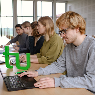 Fünf Studierende im Seminarraum sitzen in einer Tischreihe und sehen auf ihren Laptop.