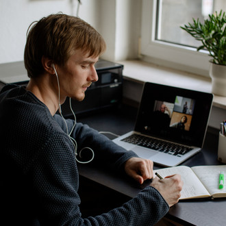 Ein Student arbeitet mit Laptop und Notizbuch.