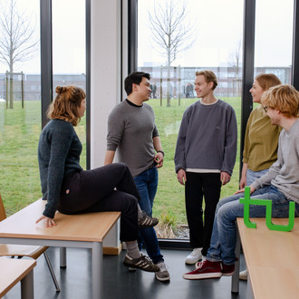 Ein Gruppenfoto von Studierenden im Seminarraum mit dem TU Dortmund Logo. Sie sprechen miteinander und schauen sich an.