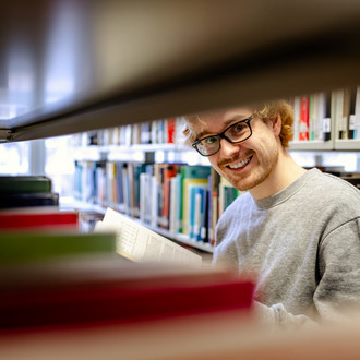 Ein Studierender steht an einem Bücherregal in der Bibliothek.