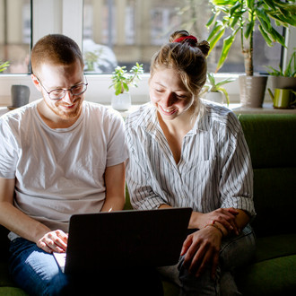 Zwei Studierende arbeiten am Laptop, auf einem Sofa sitzend.