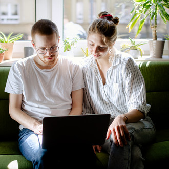 Zwei Studierende arbeiten am Laptop, auf einem Sofa sitzend.