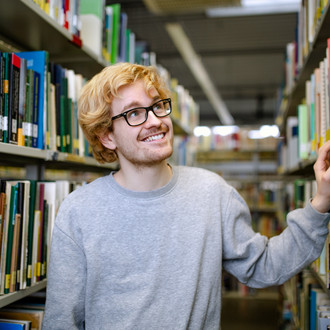 Studierender steht suchend an einem Bücherregal in der Bibliothek.