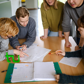 Fünf Studierende im Seminarraum um einen Tisch herum und sehen auf ein Dokument