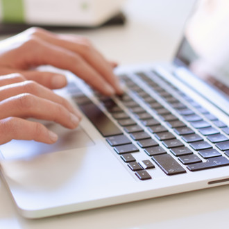 Studentin tippend am Laptop, daneben liegen Bücher.