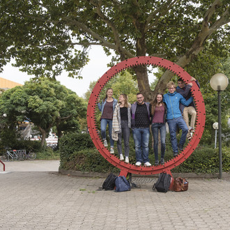 Studierende stehen gemeinsam in einem roten Zahnrad.