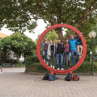Studierende stehen gemeinsam in einem roten Zahnrad.