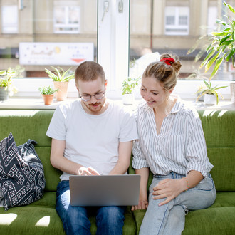 Zwei Studierende arbeiten am Laptop, auf einem Sofa sitzend.