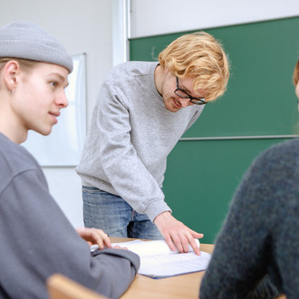 Drei Studierende im Seminarraum arbeiten zusammen.