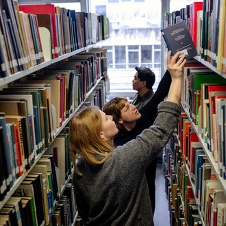 Studierende suchen nach Büchern in Bücherregalen in der Bibliothek.