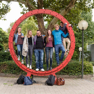 Studierende stehen gemeinsam in einem roten Zahnrad.