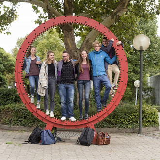 Studierende stehen gemeinsam in einem roten Zahnrad.