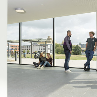 Studierende im Gespräch vor einem großen Fenster.