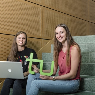 Zwei Studentinnen sitzen mit Laptop und TU-Logo auf einer Treppe.