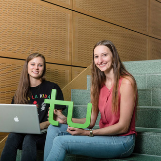 Zwei Studentinnen sitzen mit Laptop und TU-Logo auf einer Treppe.