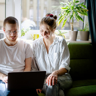 Zwei Studierende arbeiten am Laptop, auf einem Sofa sitzend.