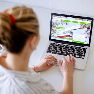 Am Schreibtisch sitzende Studentin tippt auf dem Laptop, daneben liegen Bücher und Stifte.