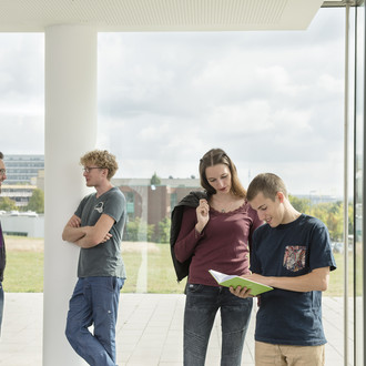 Studierende im Gespräch vor einem großen Fenster.