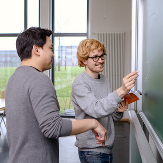 Zwei männliche Studierende schreiben etwas an die Tafel