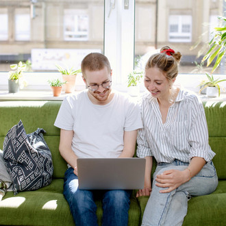 Zwei Studierende arbeiten am Laptop, auf einem Sofa sitzend.