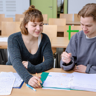 Zwei Studierende im Seminarraum arbeiten zusammen an Unterlagen.